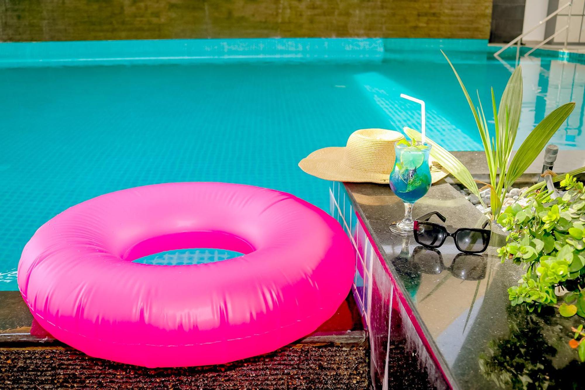 Lagoona Beach Luxury Resort And Spa Manama Eksteriør bilde The photo shows a vibrant and inviting scene by a swimming pool. In the foreground, there is a large pink inflatable float and a stylish straw hat. Next to the float, a refreshing cocktail in a glass is displayed, complete with a straw and garnishes.