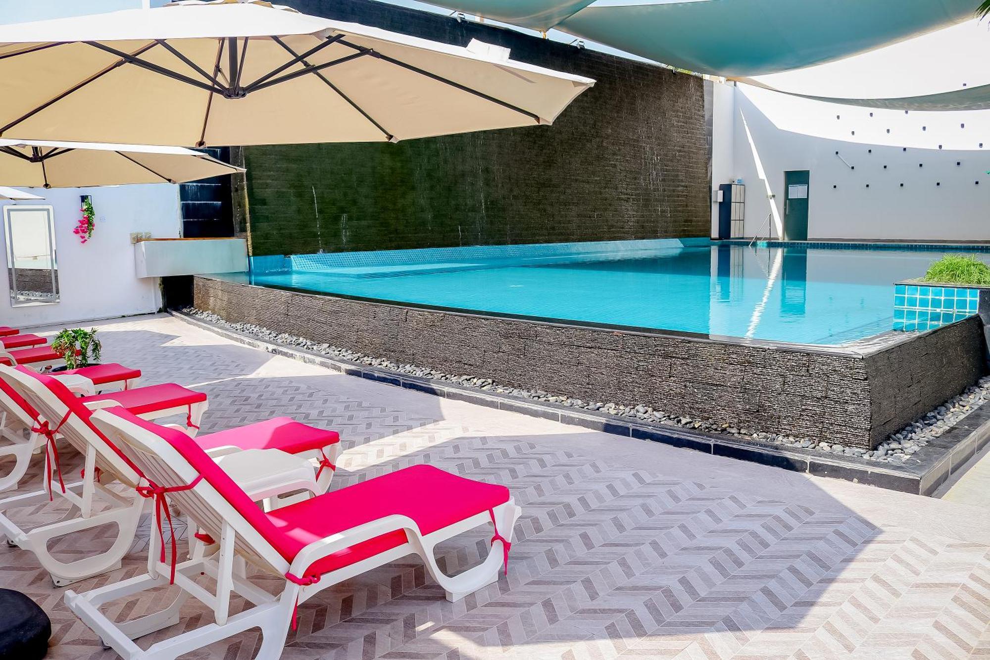 Lagoona Beach Luxury Resort And Spa Manama Eksteriør bilde The photo shows a pool area featuring a rectangular swimming pool with clear blue water. Surrounding the pool are light-colored lounge chairs with pink cushions, positioned under large umbrellas for shade. The pool is bordered by a textured wall, and