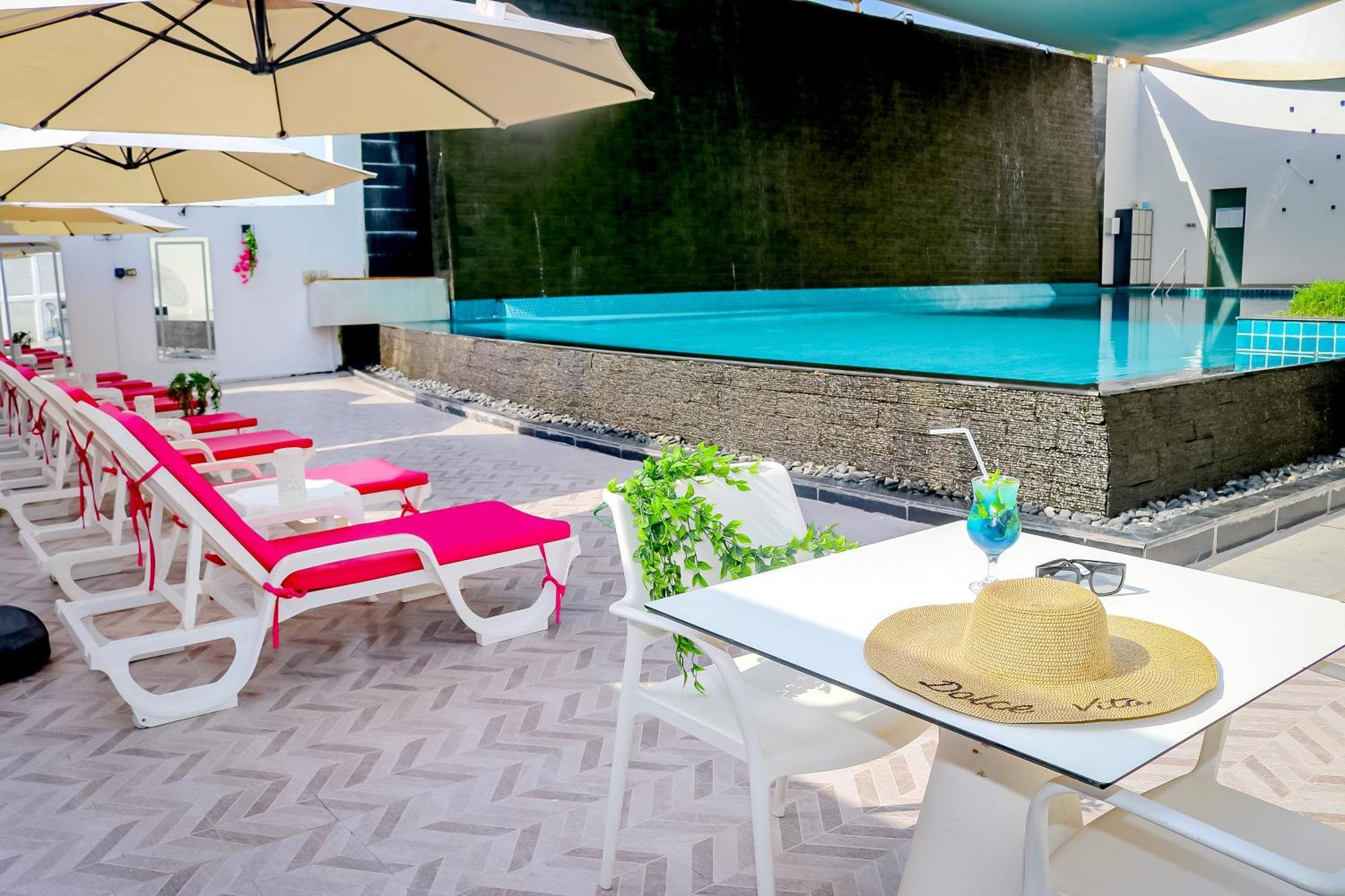 Lagoona Beach Luxury Resort And Spa Manama Eksteriør bilde The photo shows a sunny poolside area with bright red lounge chairs arranged neatly beside a swimming pool. There are large beige umbrellas providing shade. A small table is set up with a straw hat and a colorful drink, suggesting a relaxed, tropical