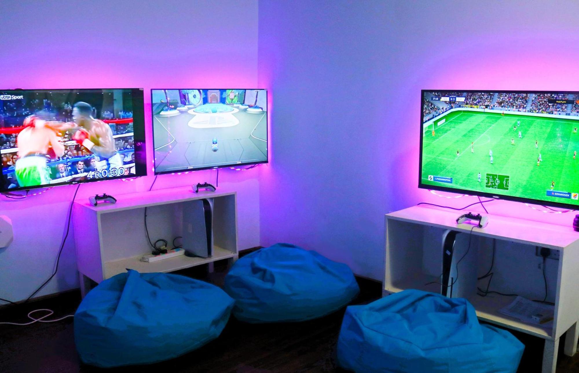 Lagoona Beach Luxury Resort And Spa Manama Eksteriør bilde The photo shows a gaming area featuring three televisions mounted on the wall, displaying different games. Two of the TVs are showing gaming scenes, with one depicting a boxing game and the other showing a vibrant game environment. The third TV displ