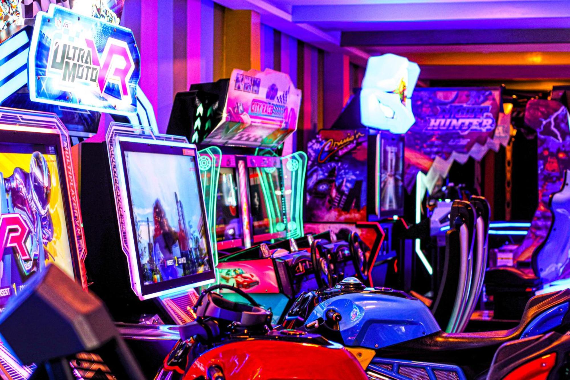 Lagoona Beach Luxury Resort And Spa Manama Eksteriør bilde The photo shows a vibrant arcade scene featuring various arcade gaming machines. The machines are lined up, showcasing colorful screens and bright, neon lights, creating an energetic atmosphere. Some machines appear to be racing games, as indicated b