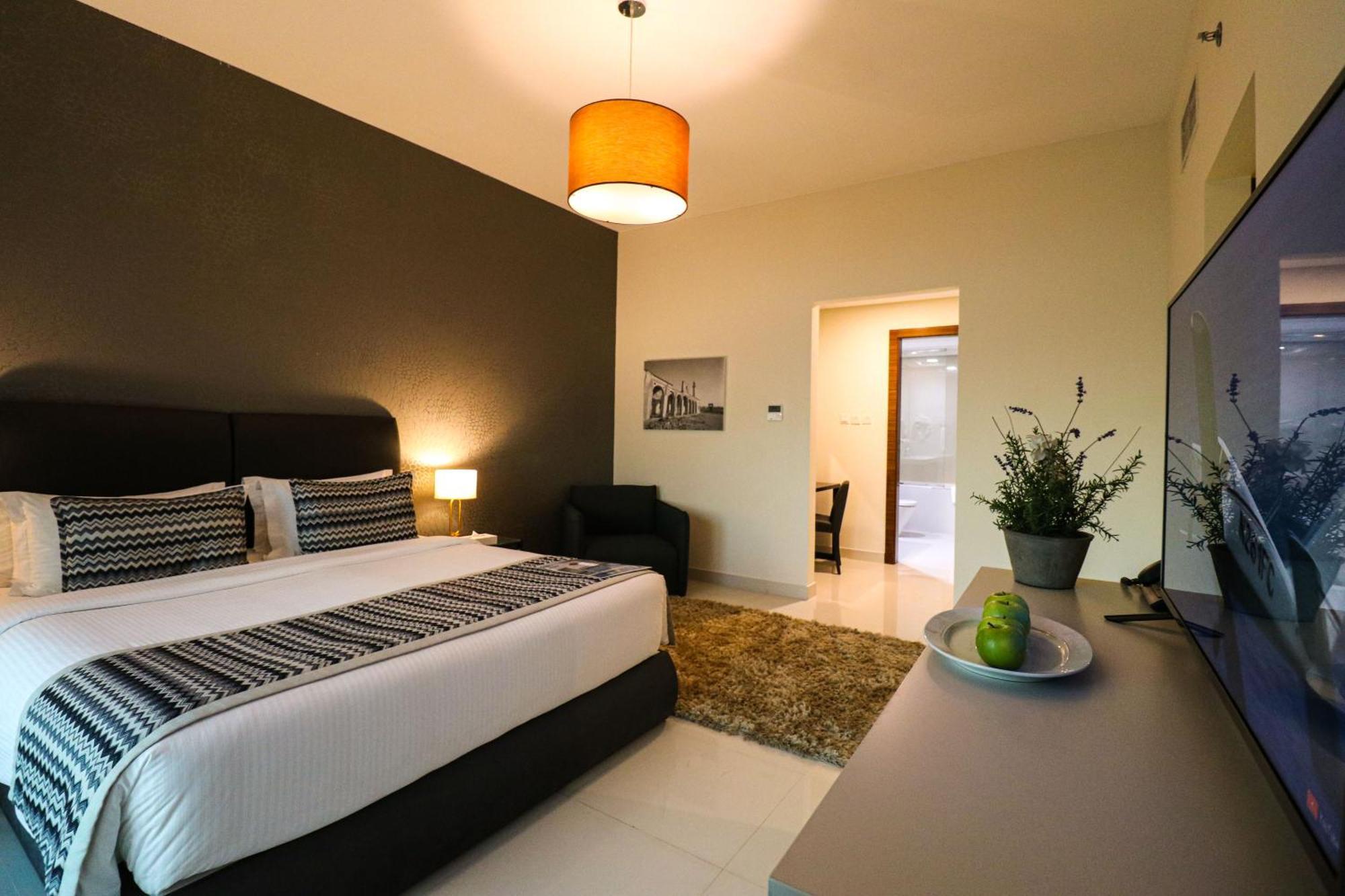 Lagoona Beach Luxury Resort And Spa Manama Eksteriør bilde The photo shows a modern hotel room. It features a large bed with a neatly made white and dark-colored duvet. On either side of the bed, there are bedside tables with lamps. The wall behind the bed is painted in a dark color, creating a contrast with