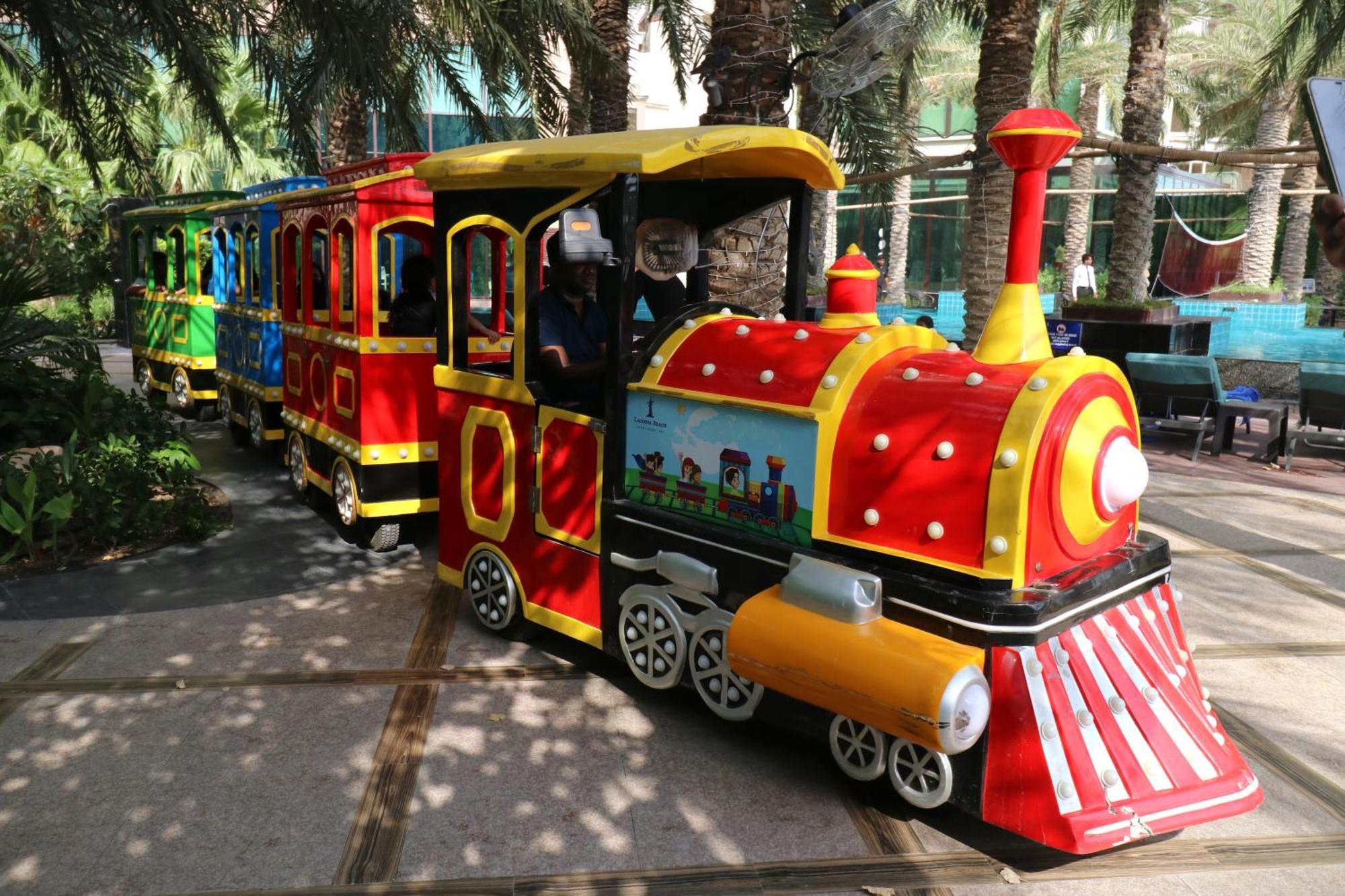 Lagoona Beach Luxury Resort And Spa Manama Eksteriør bilde The photo shows a colorful miniature train. It features a vibrant design with bright red, yellow, and blue colors. The front of the train resembles a classic steam engine, complete with a prominent smokestack. The train is designed to resemble a fun 