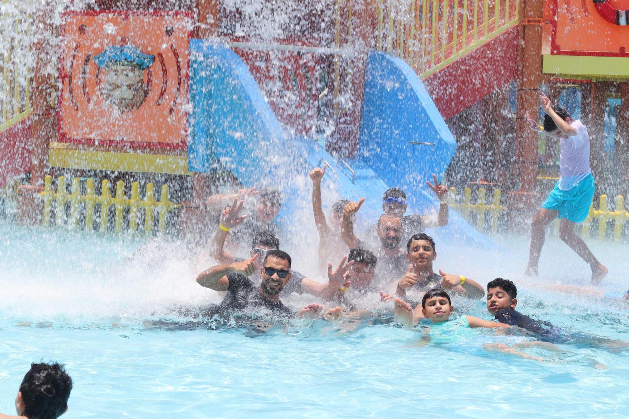 Lagoona Beach Luxury Resort And Spa Manama Eksteriør bilde The photo shows a lively scene at a water park or pool area. Several people, including adults and children, are enjoying themselves in the water, splashing and posing for the camera. Water is cascading down, creating a refreshing atmosphere. In the b