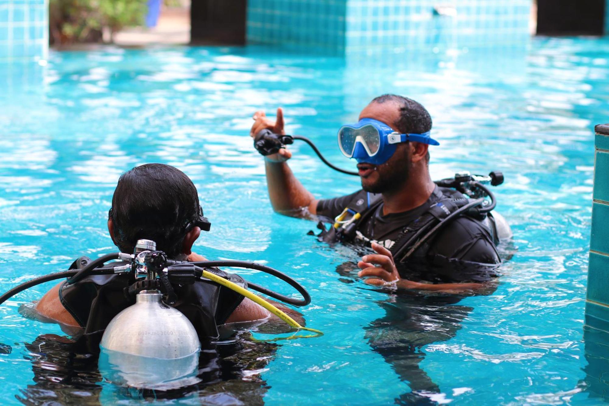 Lagoona Beach Luxury Resort And Spa Manama Eksteriør bilde The photo shows two divers in a pool. One diver is wearing a scuba mask and is speaking to the other diver, who is also equipped with scuba gear. They appear to be engaged in a discussion, possibly related to diving instructions or safety. The water 