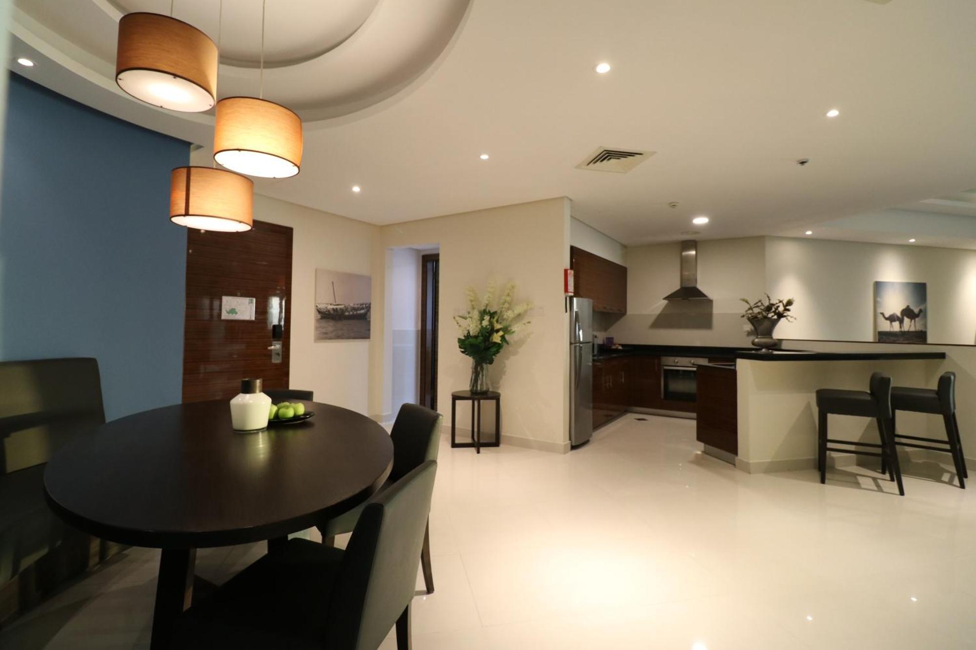 Lagoona Beach Luxury Resort And Spa Manama Eksteriør bilde The photo shows a modern, open-concept dining and kitchen area. On the left, there is a round dining table with black chairs, accompanied by a few decorative elements like a small vase and some fruit. The walls have a combination of light and dark to