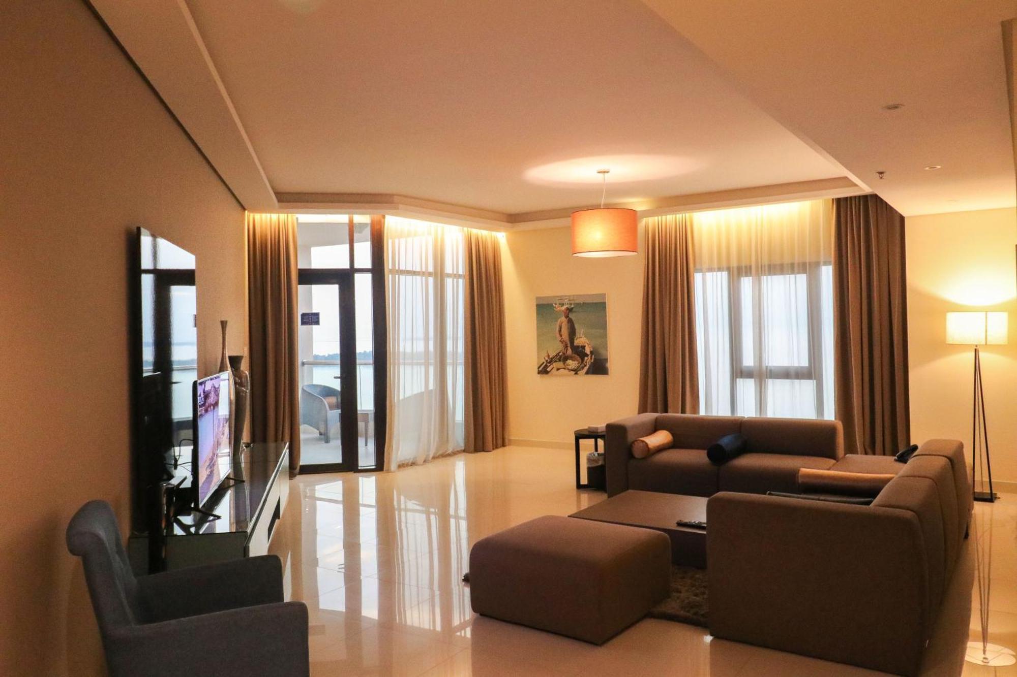Lagoona Beach Luxury Resort And Spa Manama Eksteriør bilde The photo shows a modern living room with a spacious and elegant design. It features a large couch in neutral tones, a soft ottoman, and a stylish coffee table. The walls are painted in a light color, and there are large windows with sheer curtains a