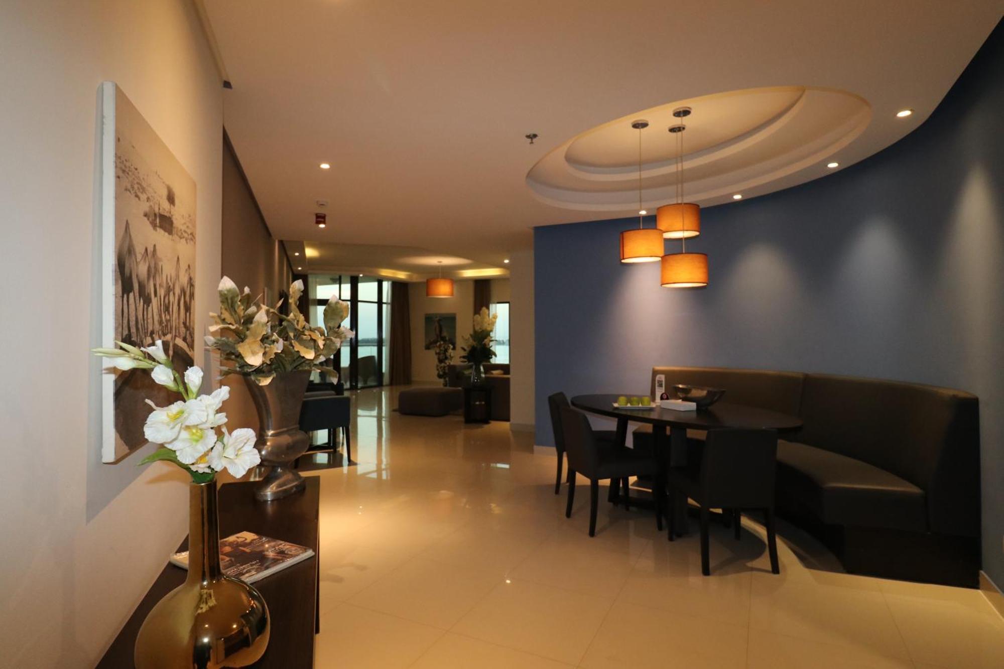 Lagoona Beach Luxury Resort And Spa Manama Eksteriør bilde The photo showcases an interior space, likely a modern lounge or reception area. It features a combination of soft lighting, neutral-colored walls, and decorative elements. There are elegant light fixtures hanging from the ceiling, and a curved blue 