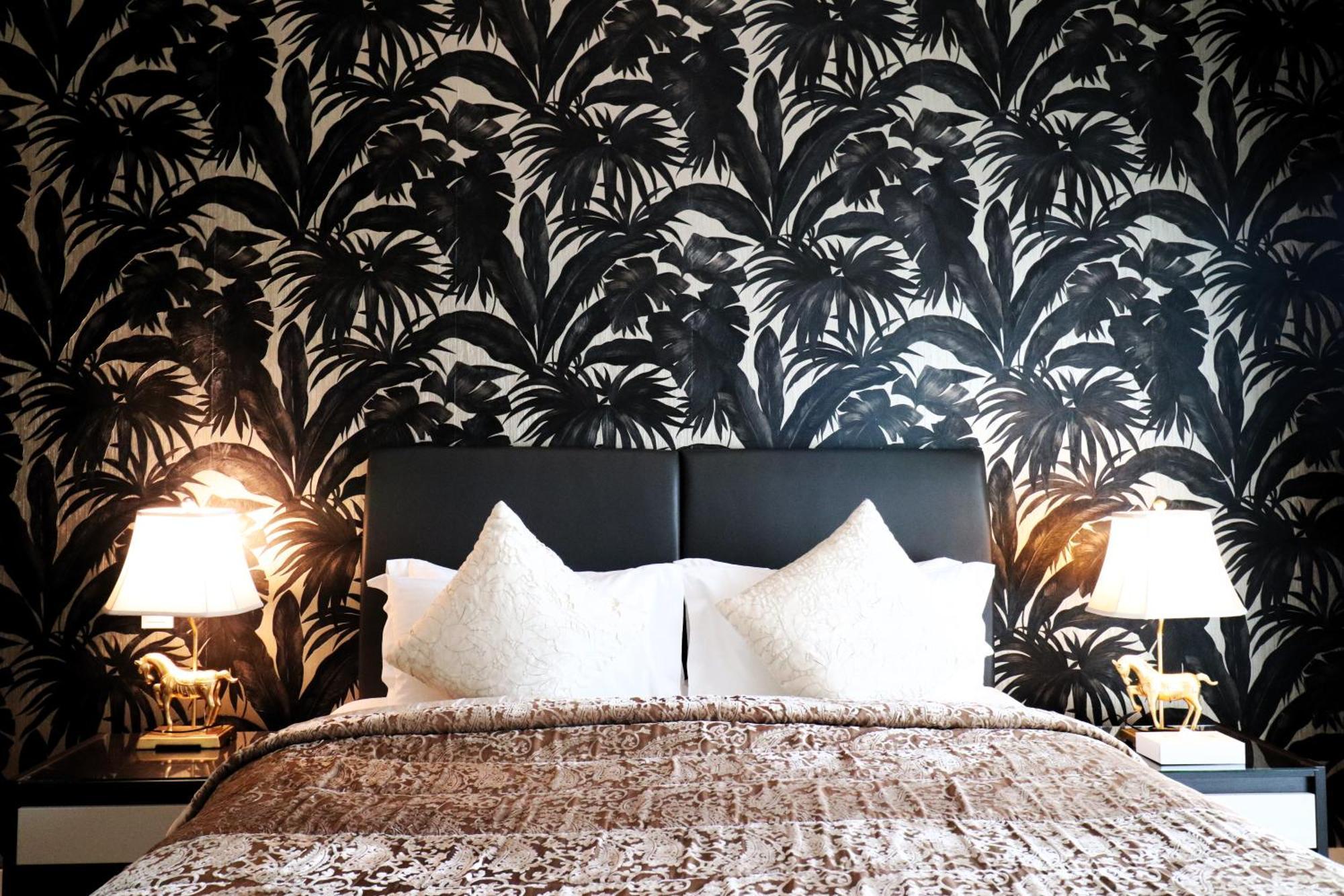Lagoona Beach Luxury Resort And Spa Manama Eksteriør bilde The photo depicts a stylish bedroom featuring a distinctive wall covered in a black and white tropical foliage wallpaper. The bed has a modern black headboard and is adorned with white pillows, creating a clean and elegant look. A textured brown thro