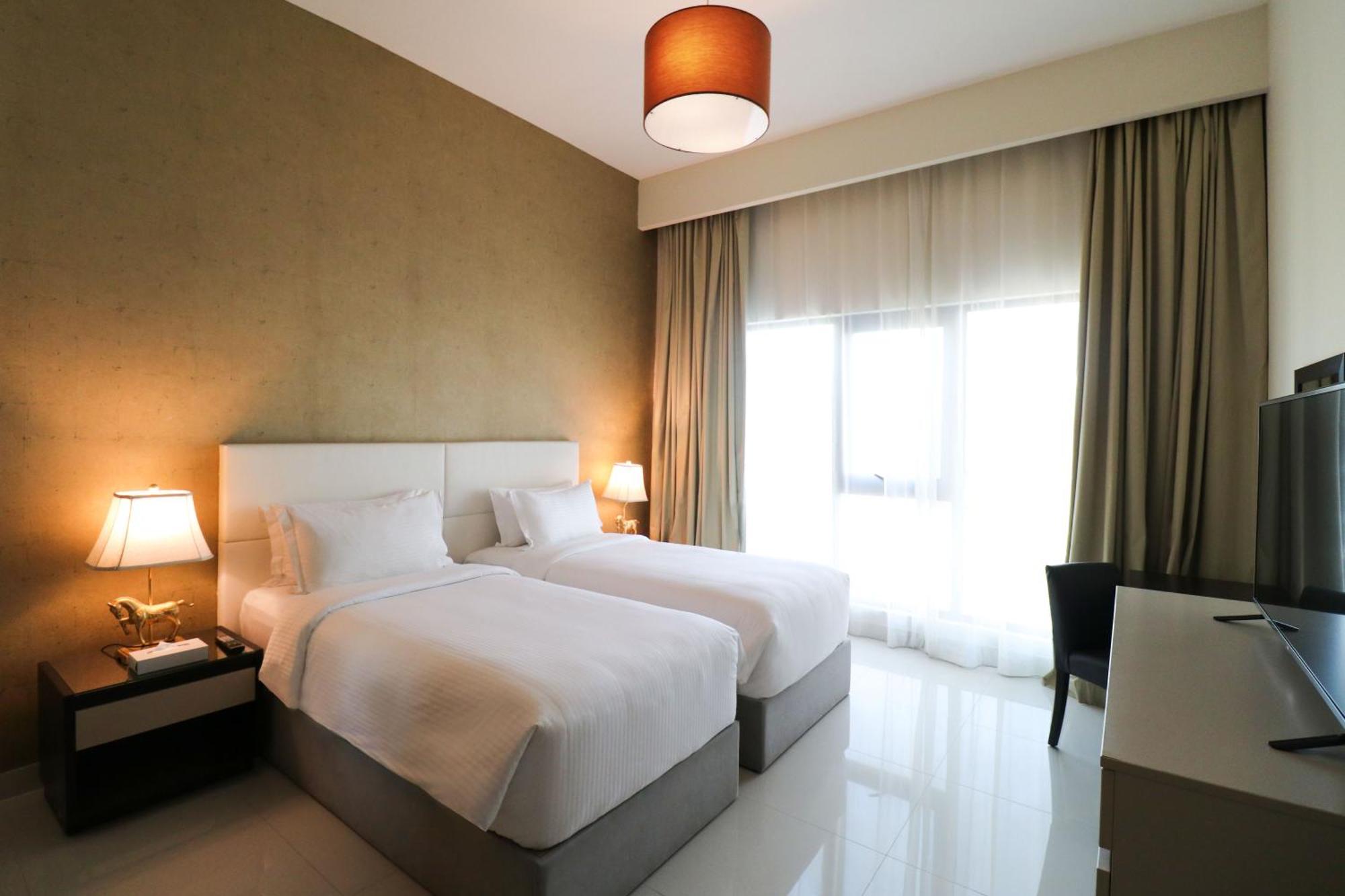 Lagoona Beach Luxury Resort And Spa Manama Eksteriør bilde The photo shows a hotel room featuring two single beds with white bedding. The walls have a neutral tone, and there's a large window covered by light, sheer curtains allowing natural light to enter. On either side of the beds, there are bedside table